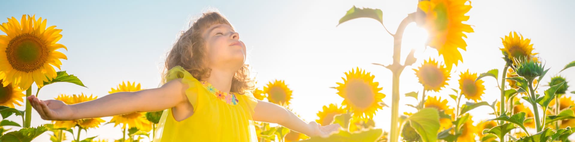 Mädchen mit ausgebreiteten Armen in einem Sonnenblumenfeld